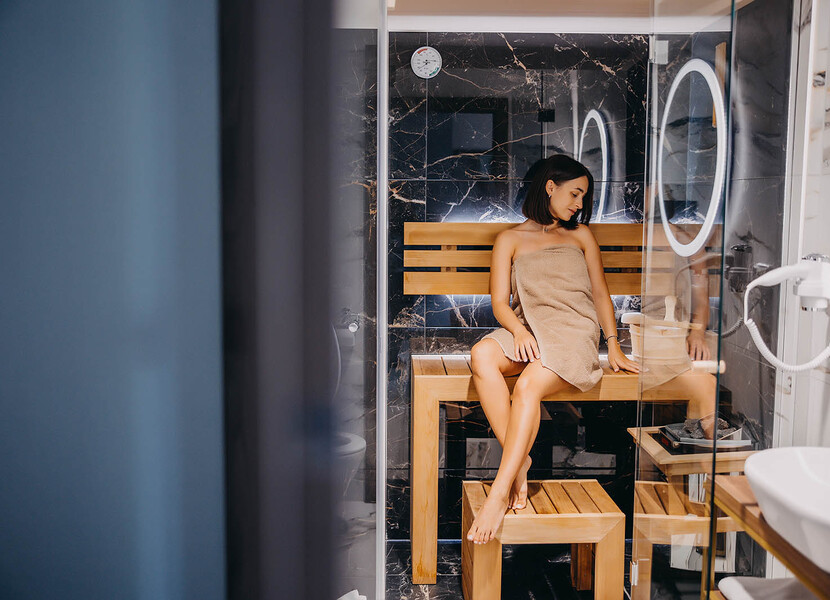 Gość relaksuje w nowoczesnej saunie z drewnianą ławką i czarnymi marmurowymi ścianami w luksusowym spa hotelowym.