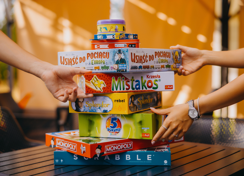 Dva lidé skládají hry na dřevěný stůl v útulném a slunném společenském prostoru