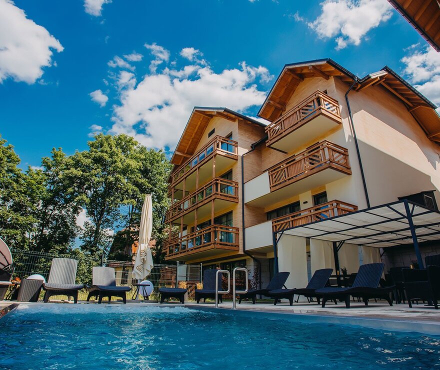 Nowoczesny hotel z drewnianymi balkonami, zewnętrznym jacuzzi, leżakami i parasolami wśród zielonych drzew