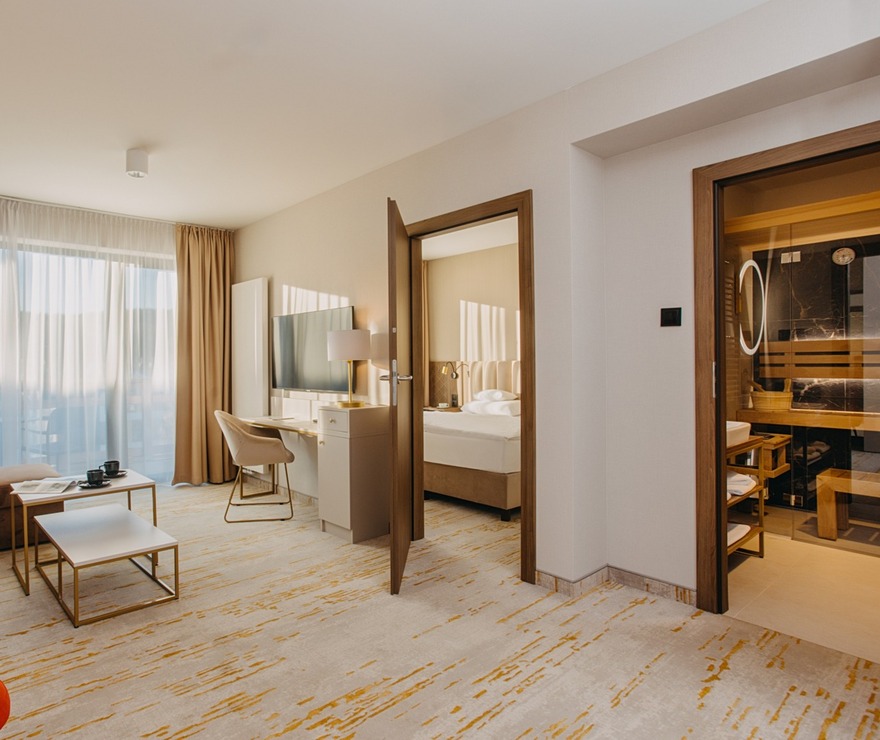 Przestronny apartament z salonem, sofą, oranżowym fotelem, biurkiem, sypialnią i sauną z widokiem przez duże okno.