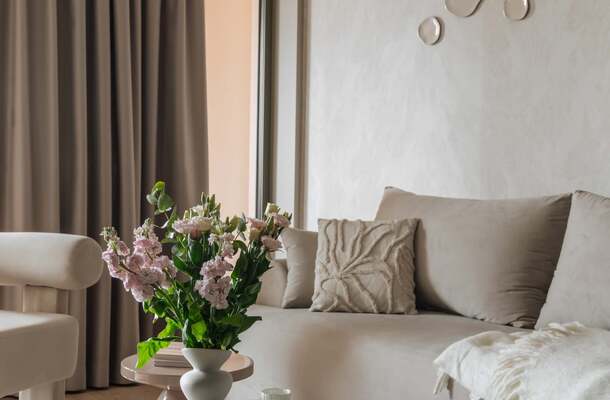 Przytulny apartament z beżową sofą, ozdobną poduszką i kocem, okrągły stolik z wazonem kwiatów, zasłony i okrągłe lustra