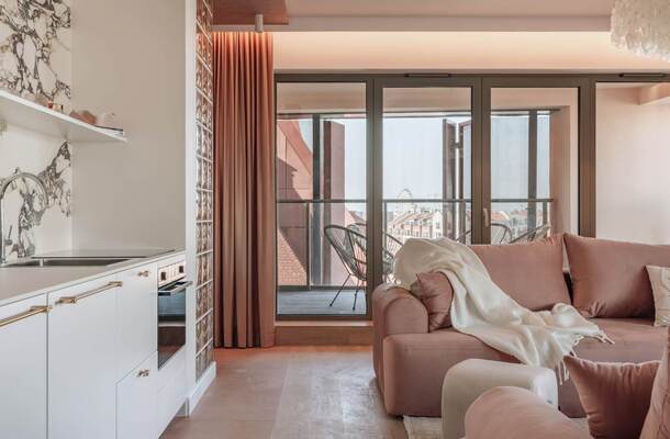 Nowoczesny apartament z aneksem kuchennym i marmurowym panelem, przytulną różową sofą z kocem i balkonem z widokiem na miasto