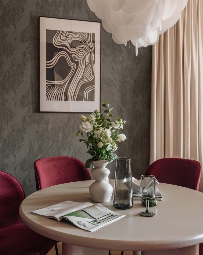 Elegancki stolik z wazonem białych kwiatów, bordowe fotele, designerska lampa i abstrakcyjna grafika na ścianie
