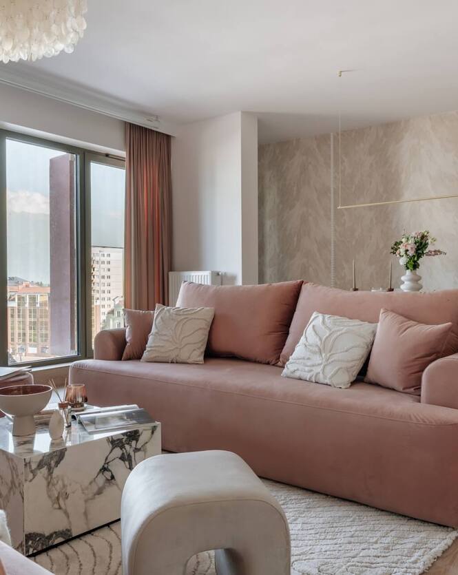 Przytulny apartament: różowa sofa, ozdobne poduszki, marmurowy stolik, duże okna z widokiem na miasto, jadalny kącik.
