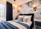 Stylowy pokój hotelowy z komfortowym łóżkiem, pikowaną wezgłowiem, geometryczną ścianą, złotymi kinkietami i biurkiem.