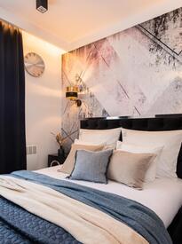 Stylowy pokój hotelowy z komfortowym łóżkiem, pikowaną wezgłowiem, geometryczną ścianą, złotymi kinkietami i biurkiem.