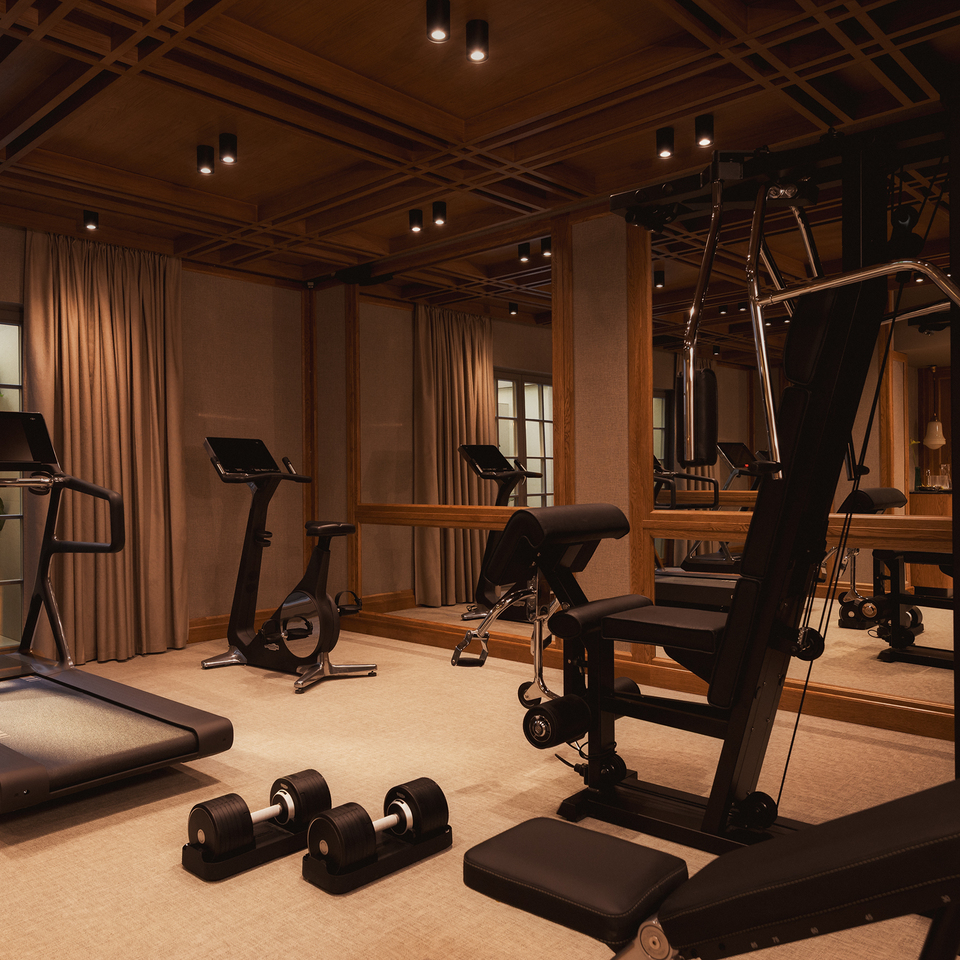 Stylowa sala fitness z bieżnią, rowerem stacjonarnym, ławką treningową i hantlami, ciepłe drewniane wykończenie