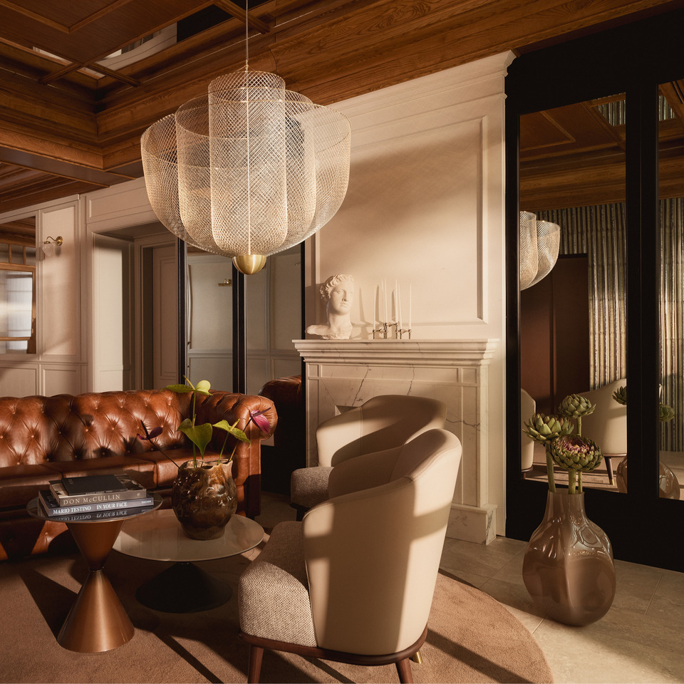 Luksusowy salon hotelowy z brązową skórzaną sofą Chesterfield, dużą ażurową lampą, marmurowym kominkiem i recepcją.
