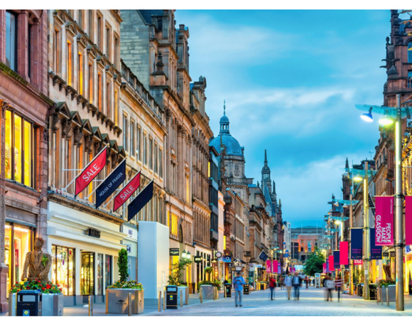 Evening pedestrian shopping street in Glasgow with historic sandstone facades, lit shop windows and café seating