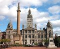 Grand historic city hall with ornate stone façade and tall central column in a spacious sunlit public square.
