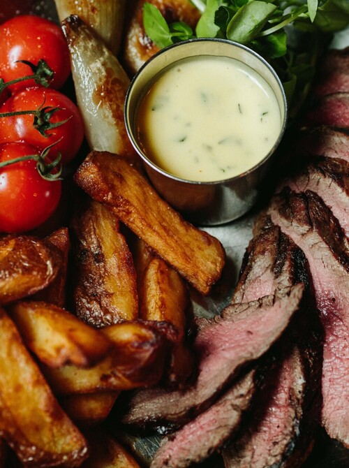 Medium-rare sliced steak with thick-cut fries, vine cherry tomatoes and herb cream sauce served in rustic skillet