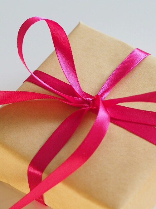 Kraft-wrapped gift box tied with a bright pink satin ribbon, styled as a hotel welcome or turndown amenity.