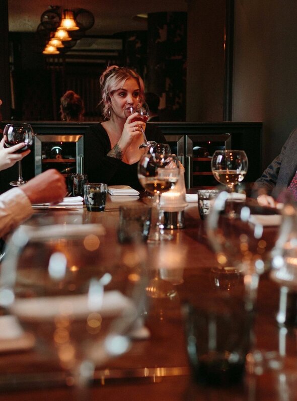 Friends enjoying wine around a candlelit hotel private dining table in an elegant, dimly lit restaurant.