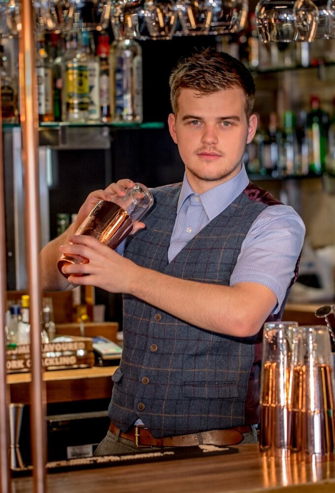 Bartender shaking a copper cocktail shaker at a stylish hotel bar with copper accents, glassware and draft taps.