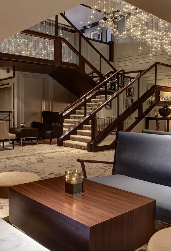 Elegant hotel lobby with grand carpeted staircase, cascading glass-bubble chandelier, plush seating and wood coffee tables.