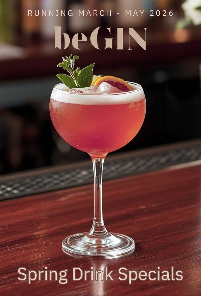 Pink gin cocktail in a coupe glass with foam, ice, mint and citrus garnish on a polished wood bar, promoting spring drink specials.