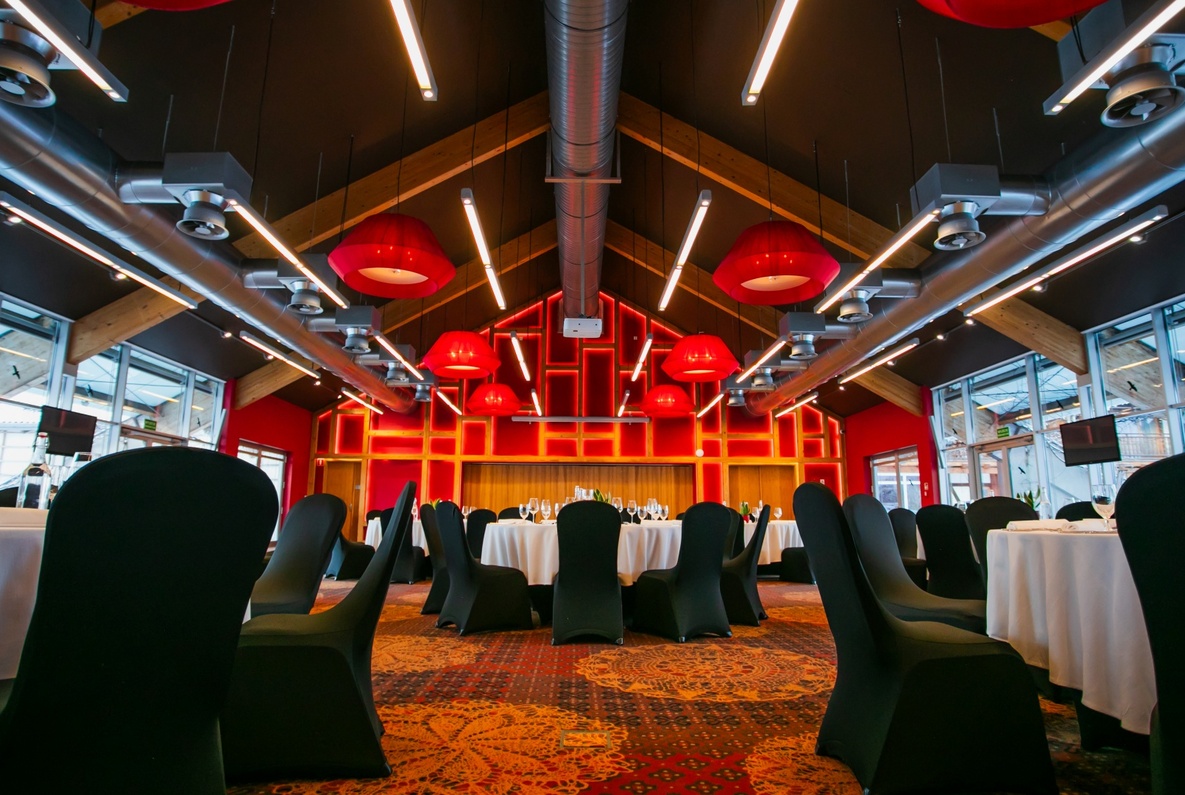 Elegant banquet hall with black chair covers, white tablecloths, and red illuminated wall panels creating a vibrant atmosphere