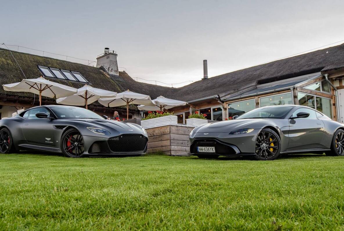 Modern hotel with traditional thatched roof, lush lawn, and luxury sports cars parked in front, suggesting upscale ambiance.