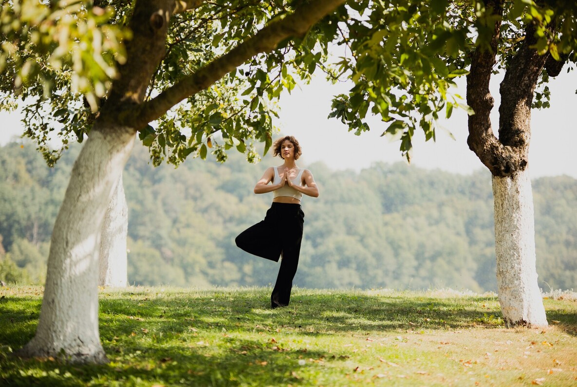 Hotelgast macht Baum-Pose im schattigen Hotelgarten zwischen Bäumen mit Blick auf bewaldetes Tal