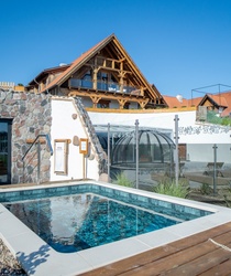 Basen z podgrzewaną wodą na zewnątrz obok kamiennej ściany i tradycyjnego drewnianego budynku z balkonem.