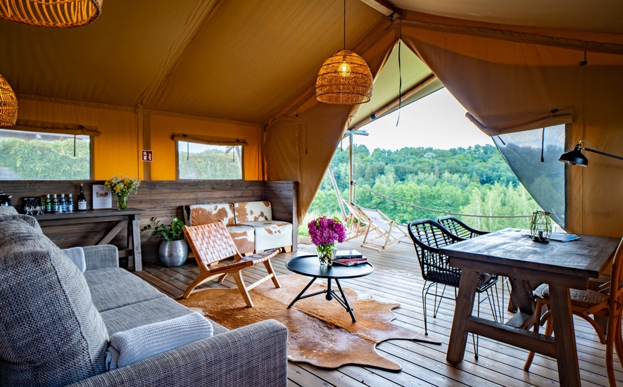 Przestronne wnętrze luksusowego namiotu glamping z wygodnymi meblami i tarasem z widokiem na zielony las.