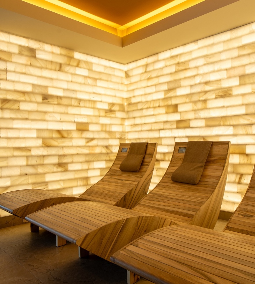 Elegant wooden lounge chairs in spa area with illuminated marble wall creating a calming, relaxing atmosphere for guests.