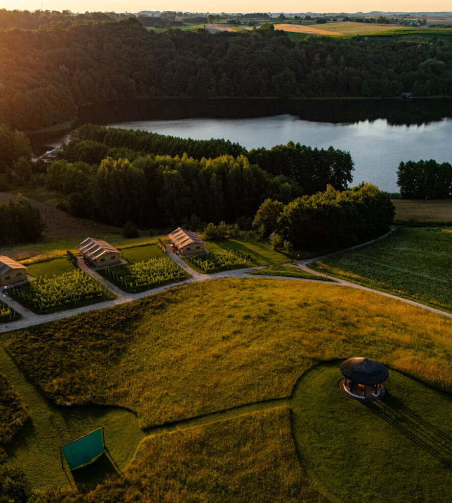Luxury tents nestled in countryside by a lake, surrounded by greenery and forest, perfect for peaceful nature retreat.