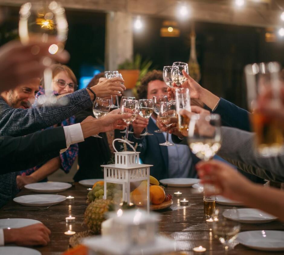 Guests raising glasses for a toast around a candlelit table decorated with fruit in a cozy, festive dining space.