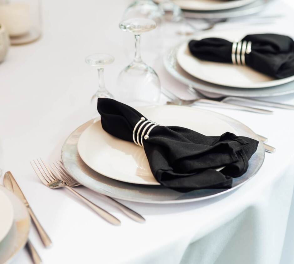 Elegantly set table with white tablecloth, white plates, black napkins with silver rings, and glassware for drinks
