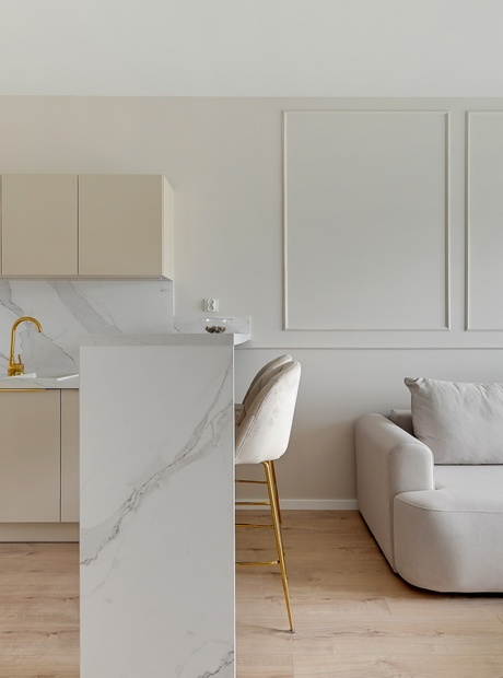 Moderne suite med åpen kjøkkenkrok, marmorbordplate og gullkran, barkrakker, myk sofa og tregulv