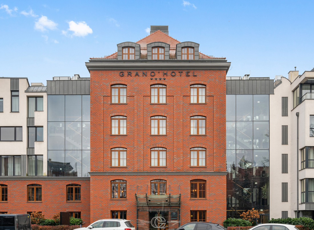 Czerwona ceglana fasada Grano Hotel z łukowymi oknami, szklanymi bocznymi skrzydłami i przeszklonym wejściem.