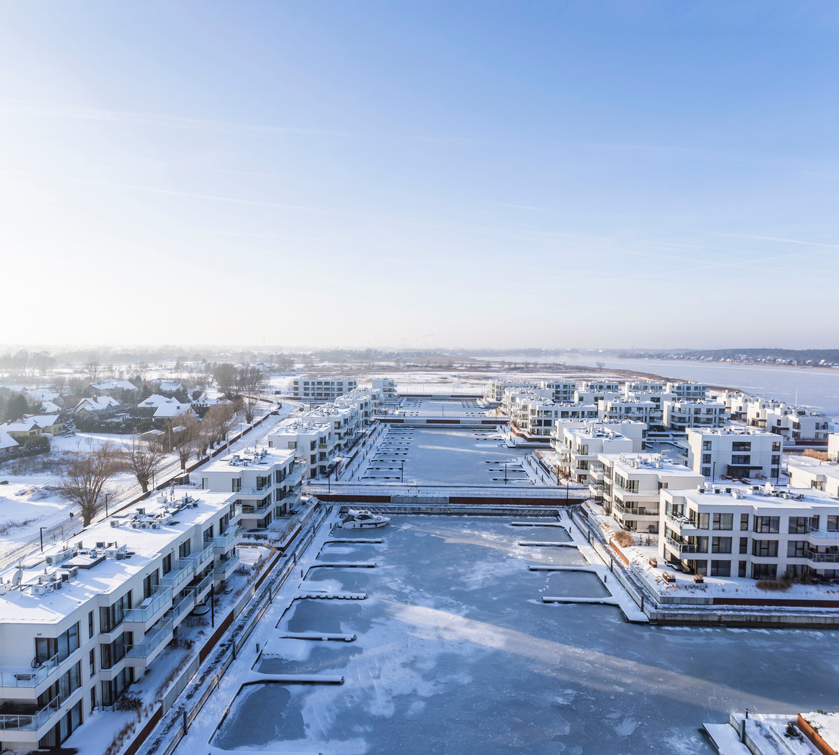 Moderna vattennära lägenheter och isbelagd marina med snötäckta terrasser och balkonger med utsikt över viken.
