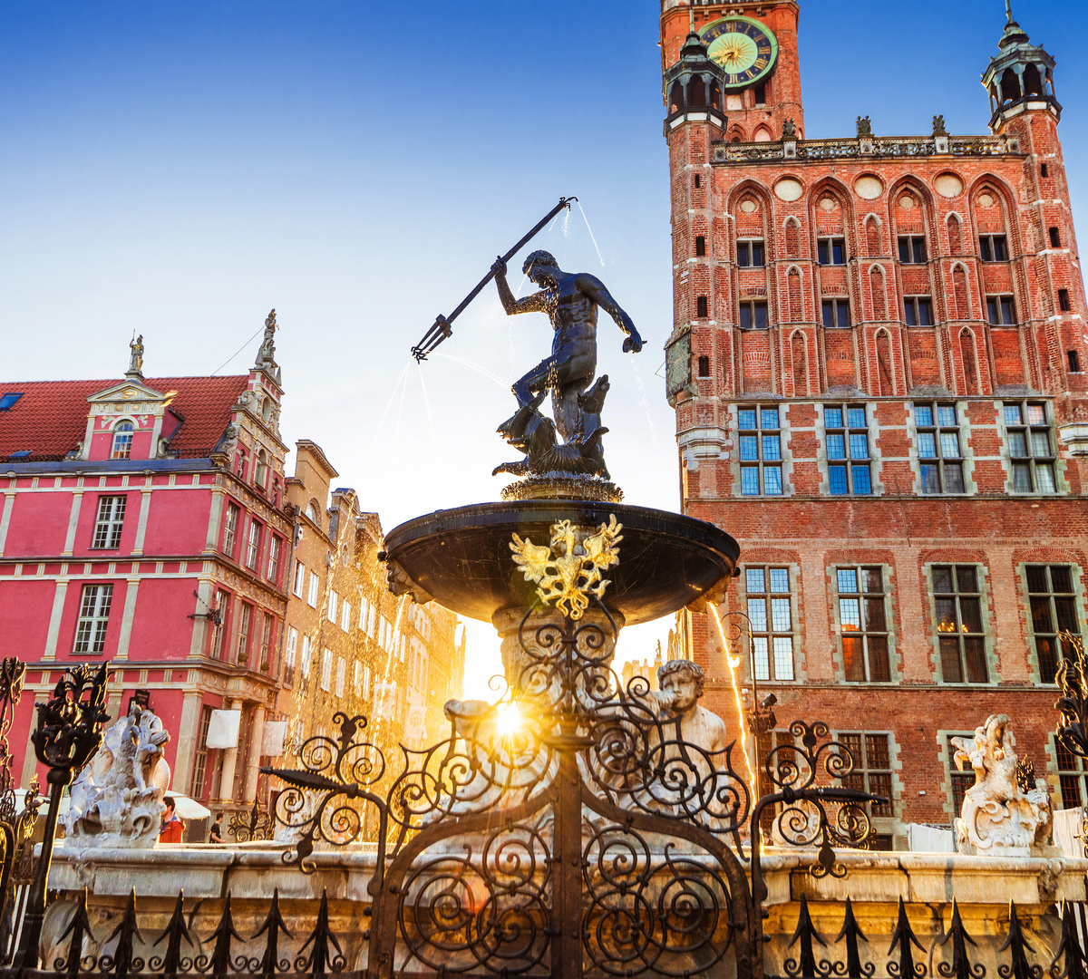 Neptune fountain in historic Gdańsk square with ornate iron fence, colorful facades and warm sunrise glow