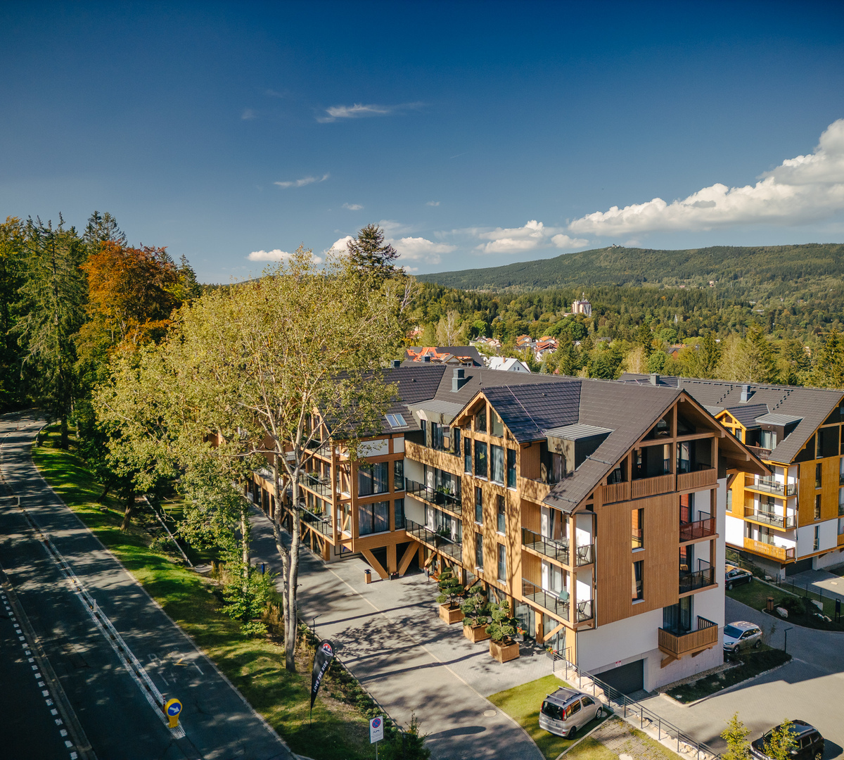 Contemporary chalet hotel with wooden balconies, mountain and forest views, outdoor parking and sunlit terraces