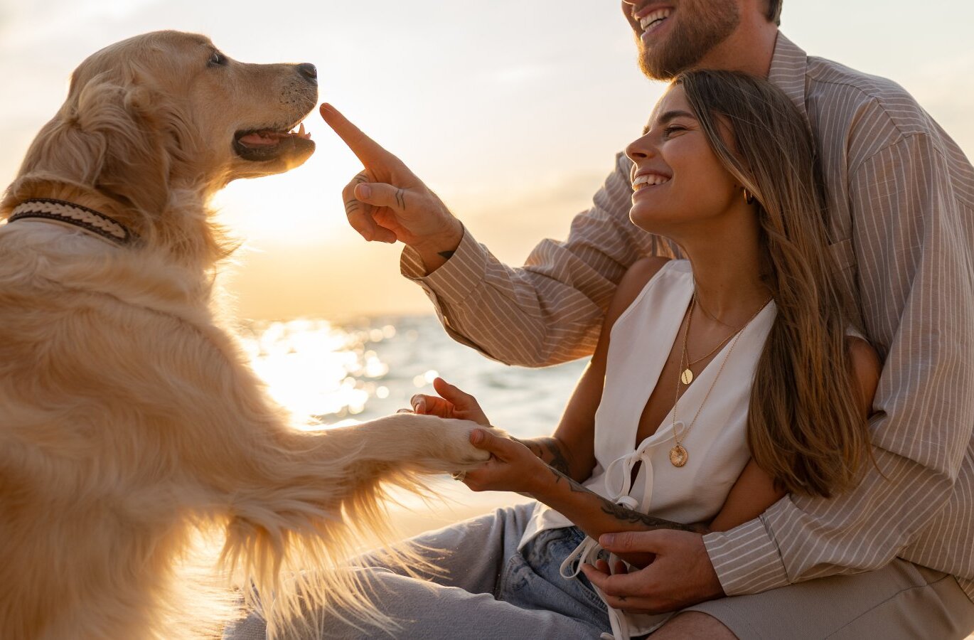 Para bawi się z golden retrieverem o zachodzie słońca na plaży, pies podaje łapę – przyjazne zwierzętom nadmorskie chwile