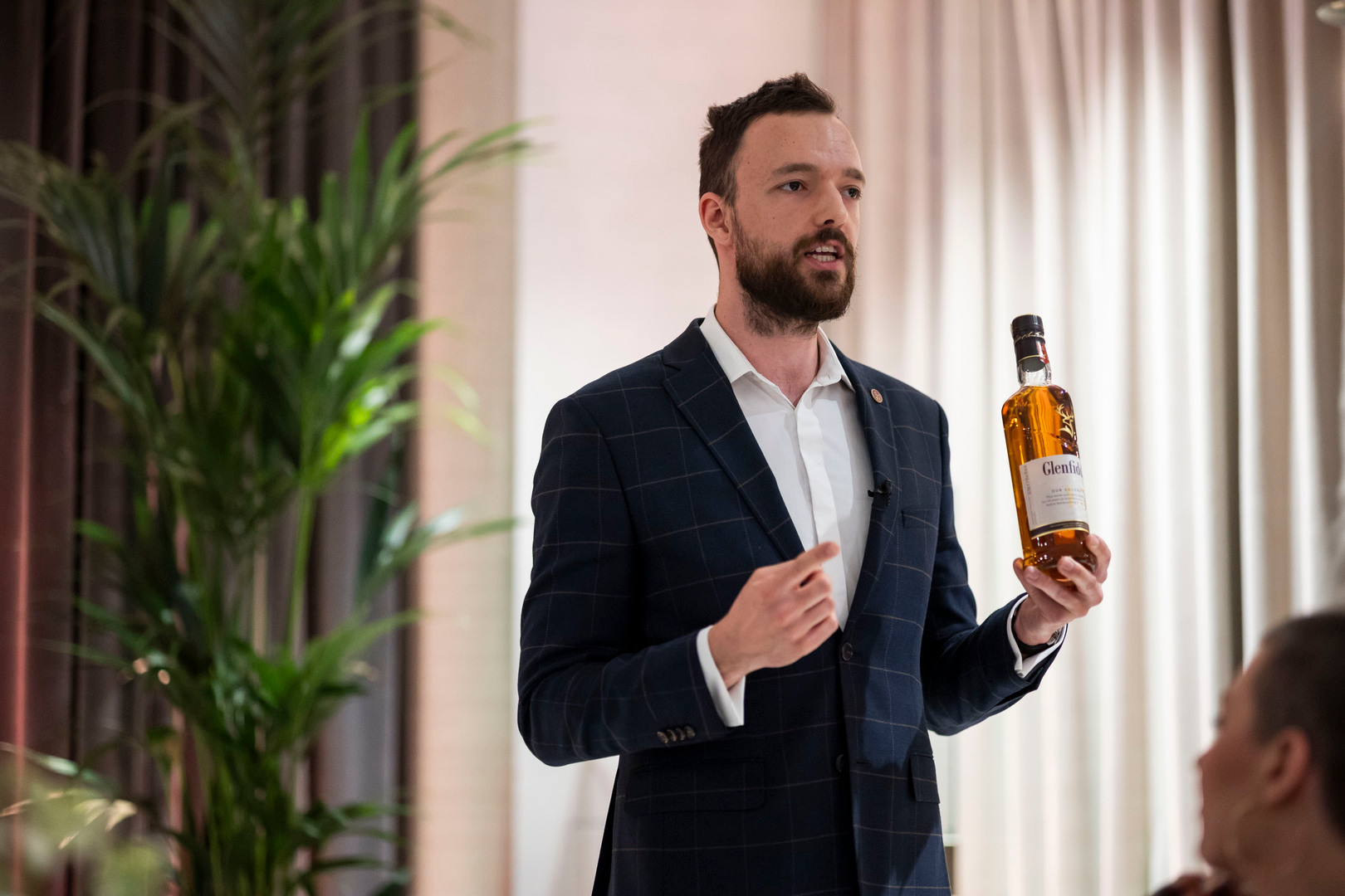 Gospodarz degustacji w eleganckim garniturze prezentuje butelkę whisky podczas kameralnej degustacji w hotelu