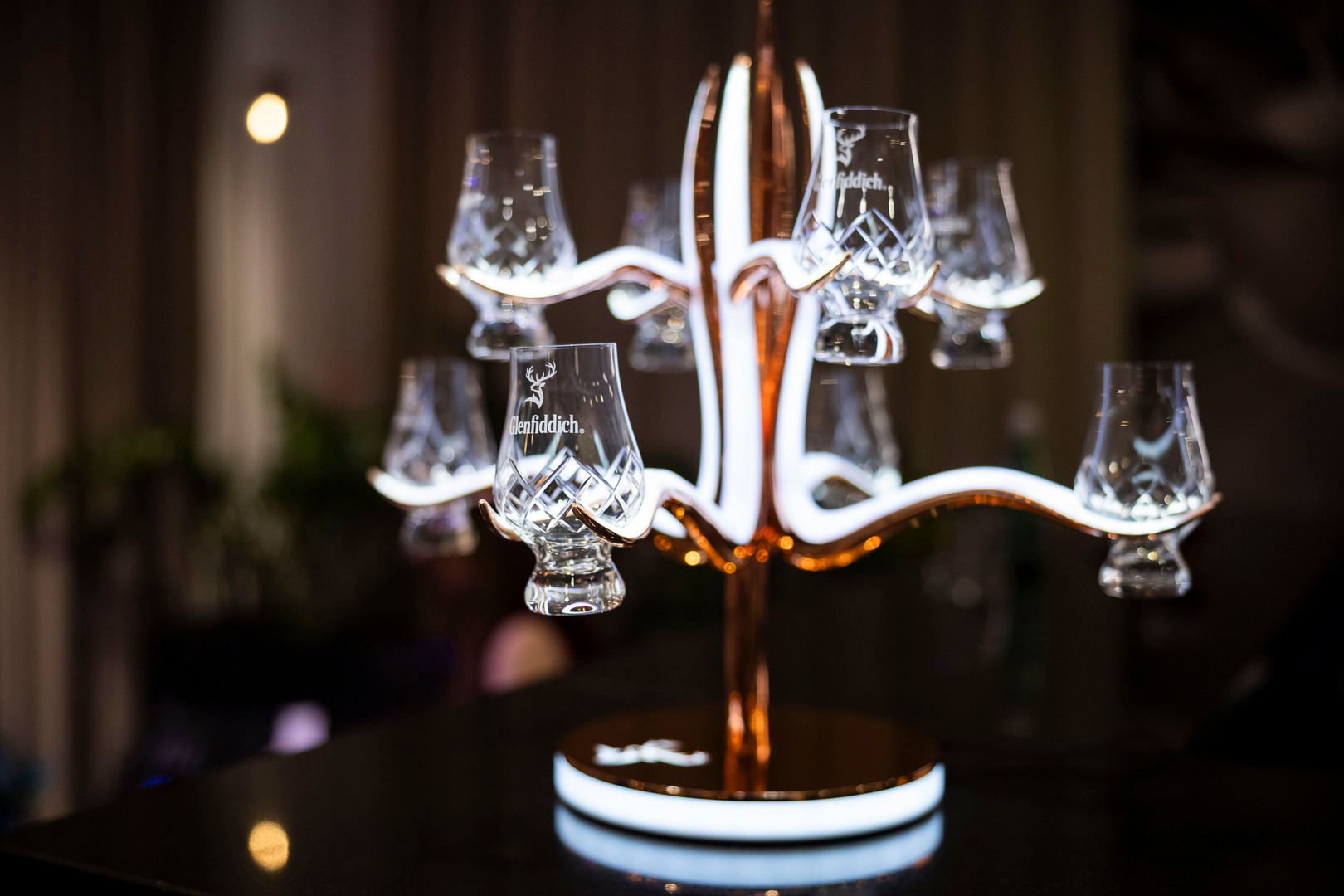 Podświetlane miedziane drzewko z kryształowymi kieliszkami degustacyjnymi Glenfiddich na barze, przytulne oświetlenie