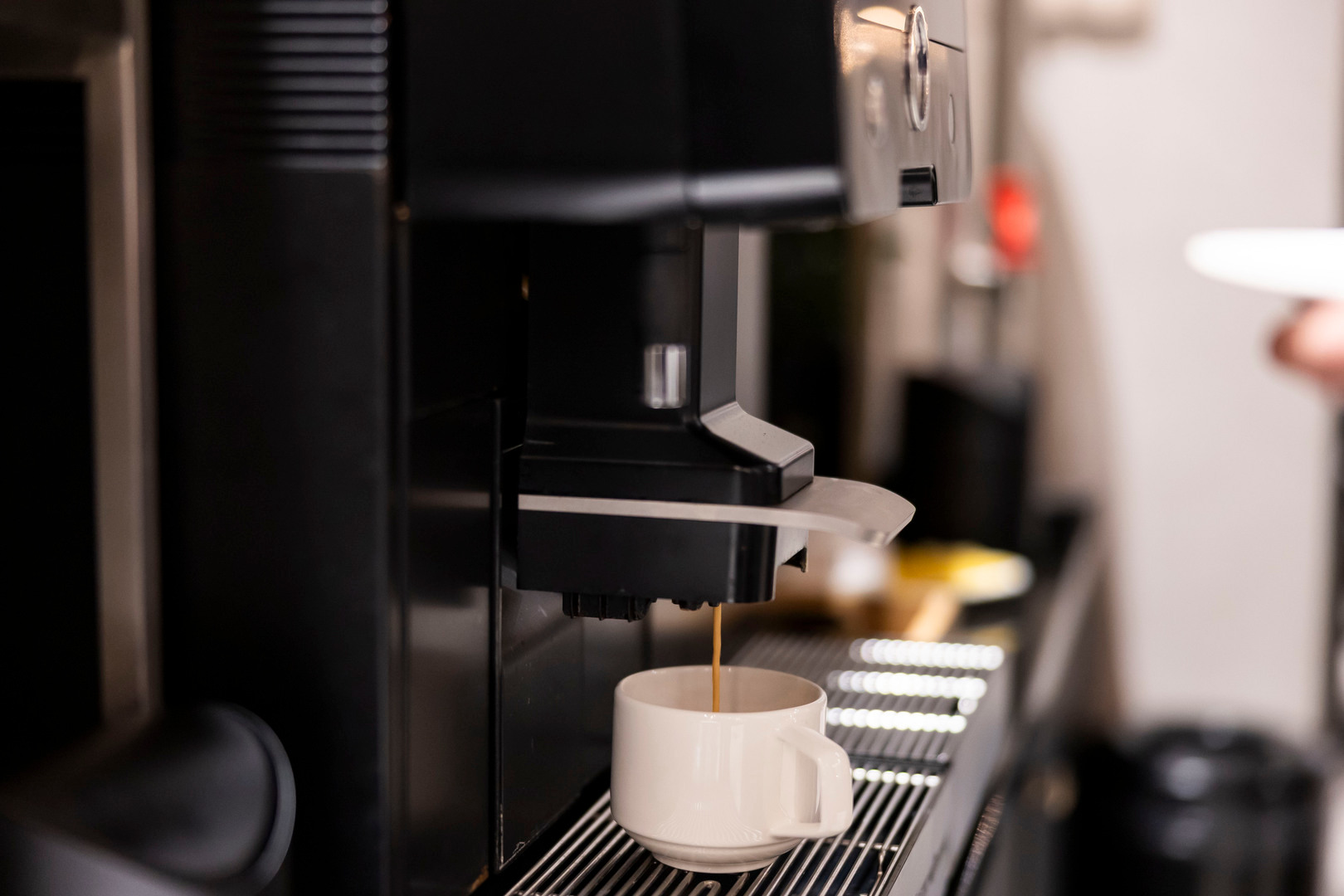 Automatyczny ekspres do espresso nalewa kawę do białego kubka na stalowym kratce w hotelowej strefie samoobsługi