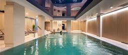 Indoor hotel spa pool with lounge chairs, cascading water jets, wood-paneled walls and guests enjoying a relaxing swim