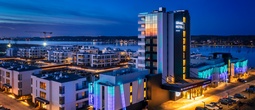Grano Hotel ved vannkanten, opplyst glassfasade med balkonger, moderne leiligheter og marina i skumring