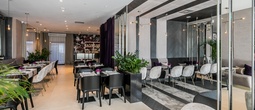 Nowoczesna restauracja hotelowa z marmurowymi stolikami, barem, nastrojowym oświetleniem, wygodnymi kanapami i roślinami