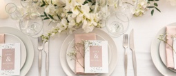 Elegant wedding table setting with white plates, blush napkin, menu card 'Anna & Michael', crystal glassware and white floral centerpiece
