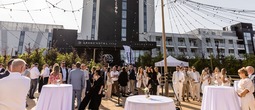Outdoor rooftop event at Grand Hotel with string lights, cocktail tables and guests mingling by modern hotel facade