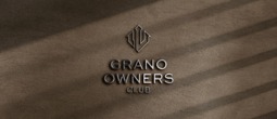 Embossed metallic GRANO OWNERS CLUB logo with geometric emblem on warm, textured brown leather-like background