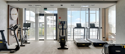 Modern hotel gym with treadmills, stationary bikes and ellipticals, floor-to-ceiling windows overlooking the marina and yachts