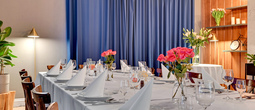 Elegant privat spiserom med langt bord i hvite duker, brettede servietter, vinglass, rosa blomsterdekor og varme treelementer