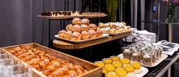 Hotelowy bufet wypieków z złotymi croissantami, lukrowanymi pączkami, różnymi ciastkami i deserami w słoiczkach.