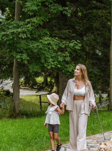 Woman and child stroll a stone path in the hotel garden with a small dog, bench and vintage lamp, peaceful family walk