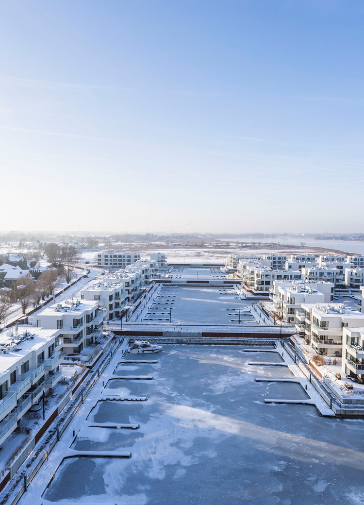 Nowoczesne nadmorskie apartamenty i zamarznięty port ze śnieżnymi tarasami i balkonami z widokiem na zatokę.