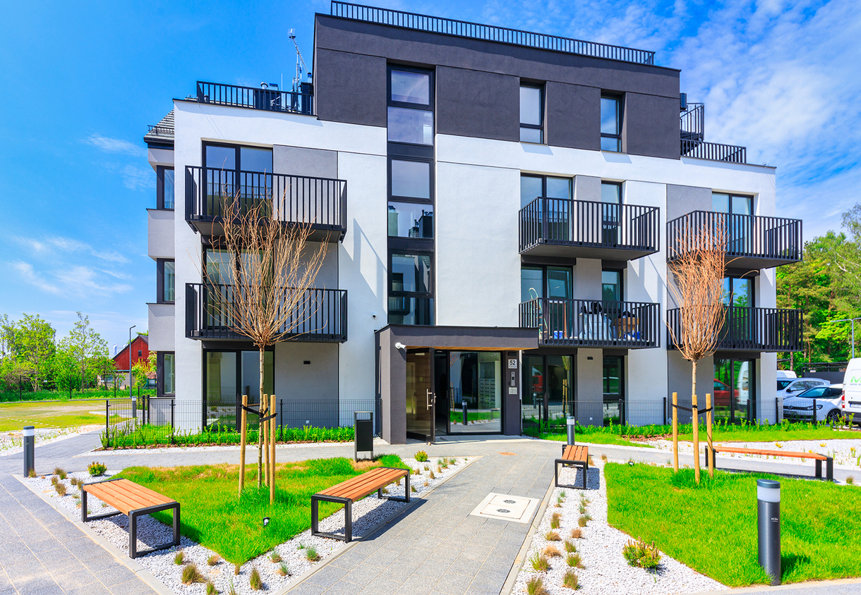 Modern aparthotel facade with private balconies, landscaped courtyard, benches, young trees and glass main entrance